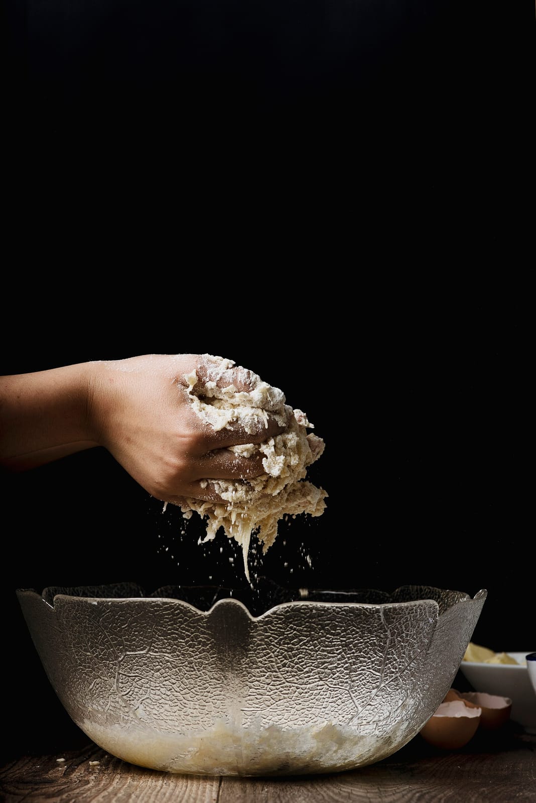 Floured hands lifting a shaggy ball of dough out of a glass mixing bowl against a dark background
