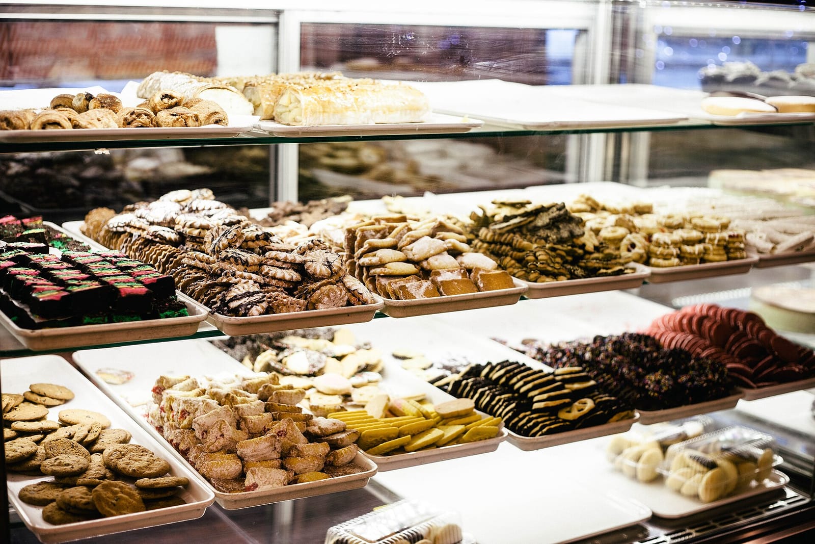 Trays of assorted cookies, bars and pastries lined up in a glass bakery case