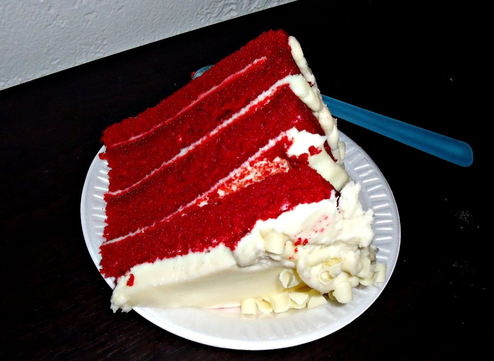 A tall slice of red velvet layer cake with white cream cheese frosting on a paper plate