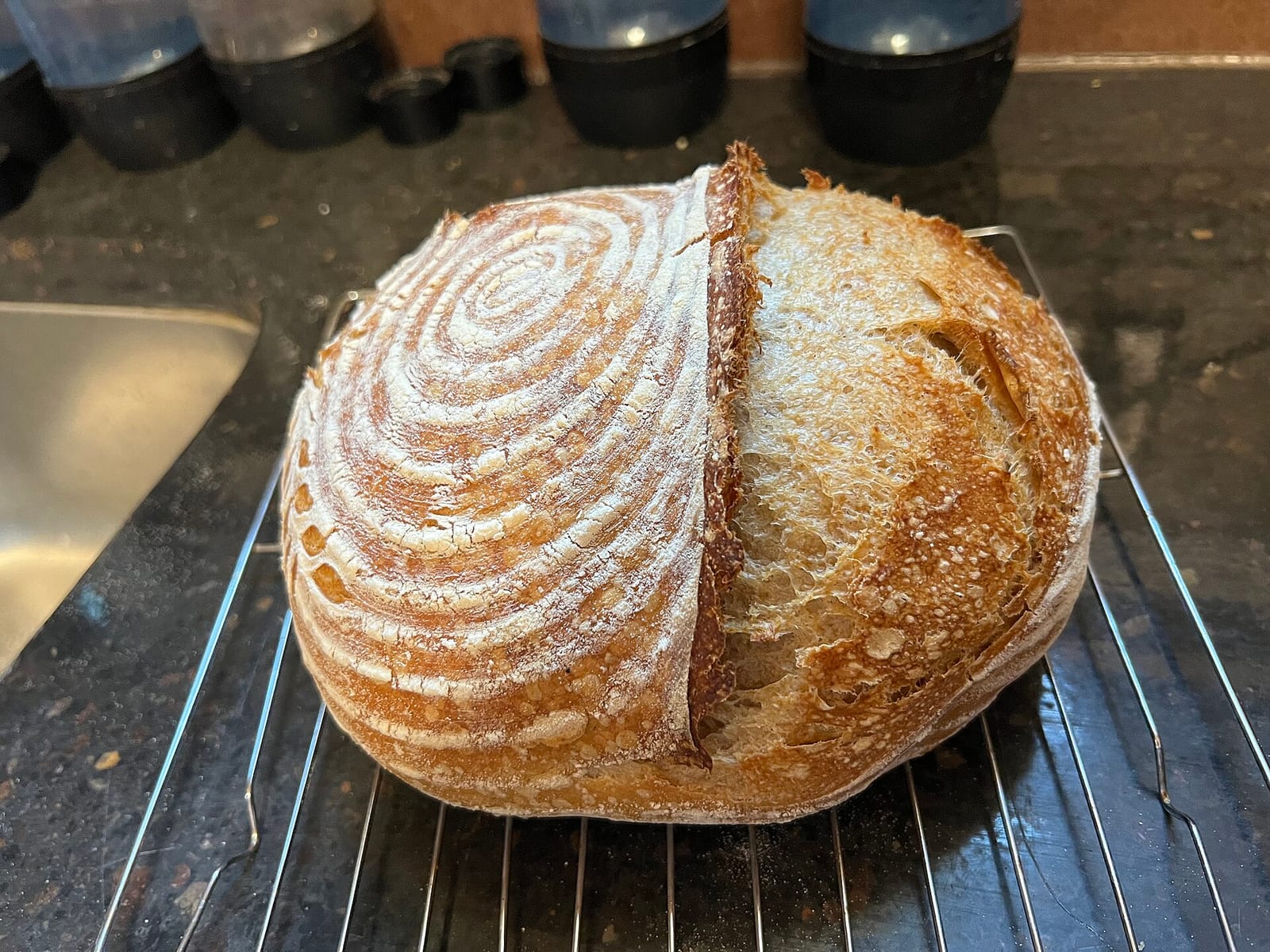 A round sourdough loaf with a spiral flour pattern and a deep ear, cooling on a wire rack